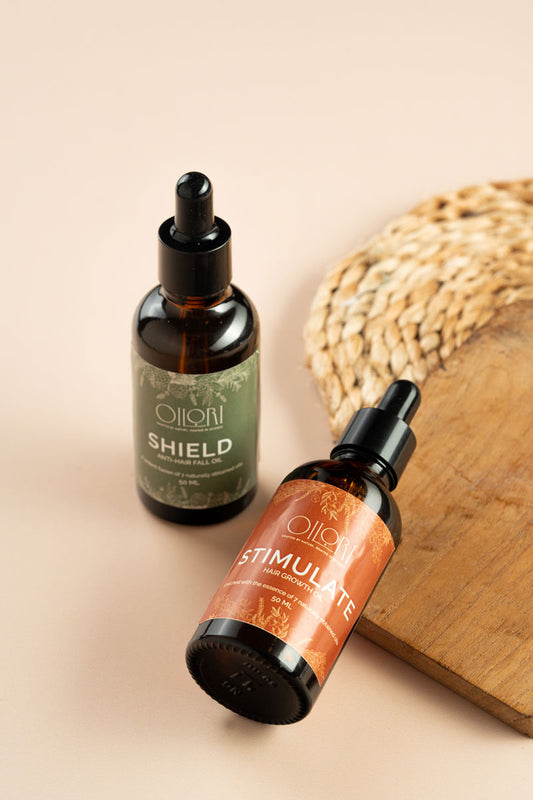 Two bottles of Oliori hair oils with 'Shield' and 'Stimulate' labels on a beige background.