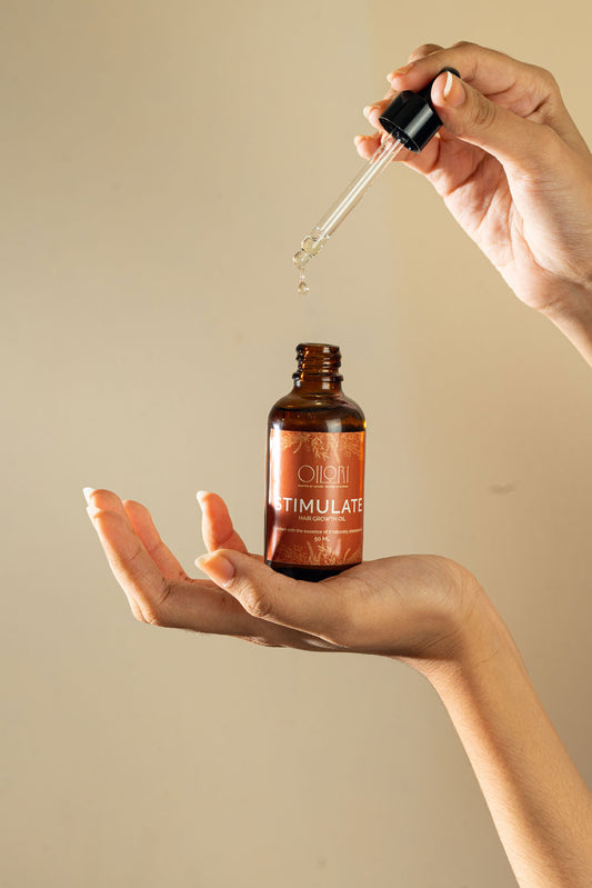 Hand holding a dropper over a bottle labeled 'Oilori with a beige background