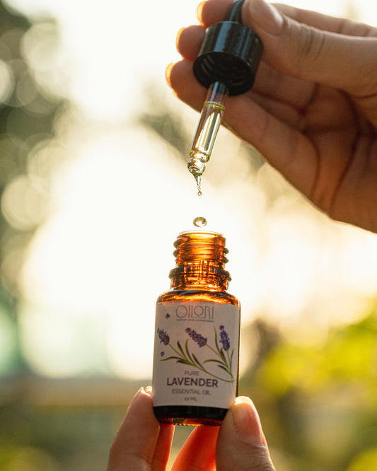Hand holding a dropper over a 10ml bottle of Oilori pure lavender essential oil with a blurred natural background